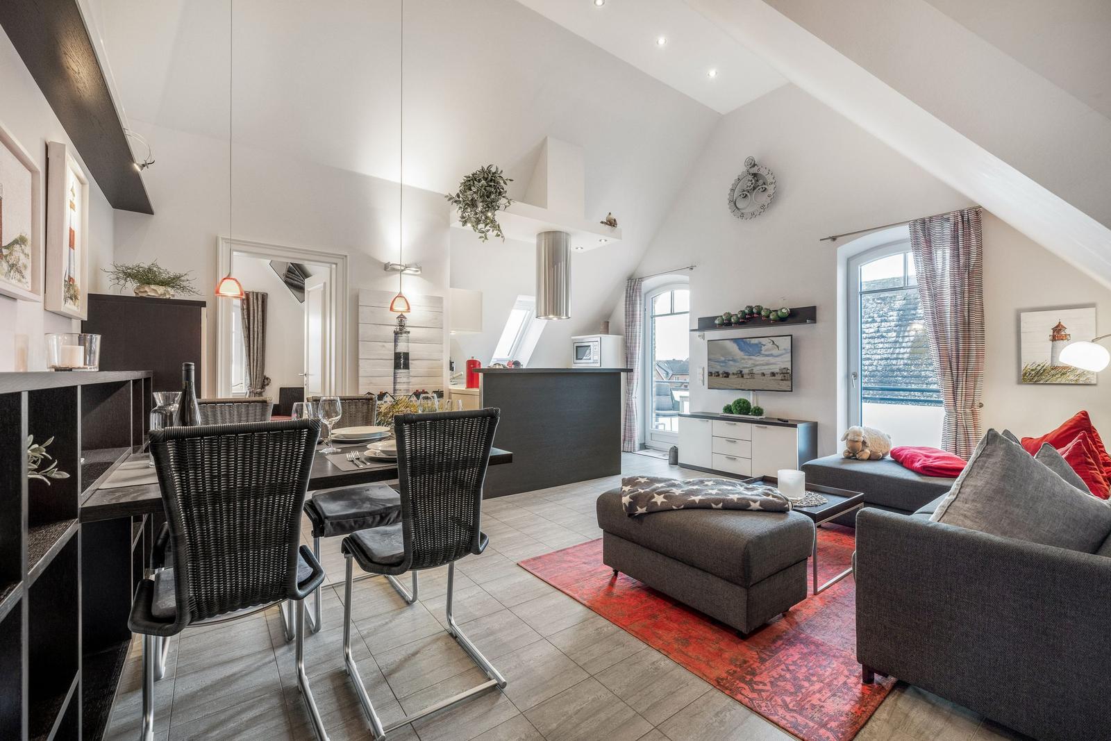 Wohn- und Essbereich mit grauer Couch, rotem Teppich und Essplatz unter hohem Dach.