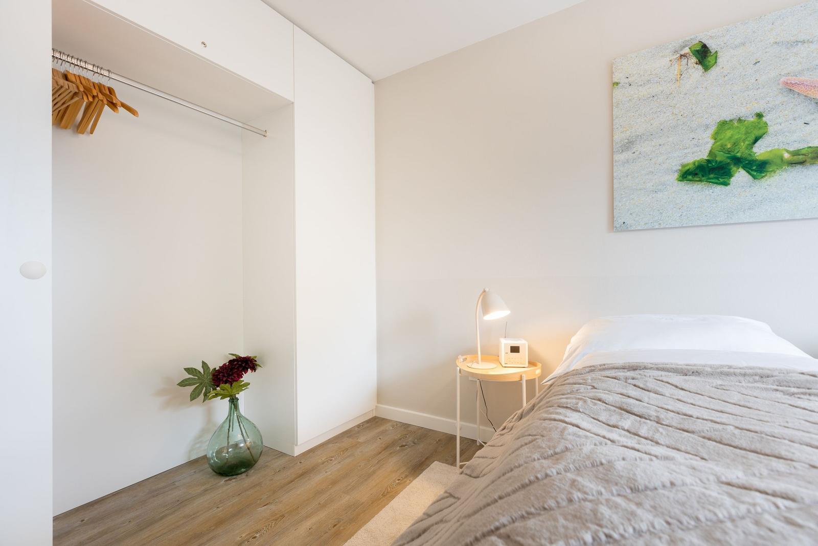 Schlafzimmer mit Bett, Nachttisch, Kleiderschrank und Wandbild.