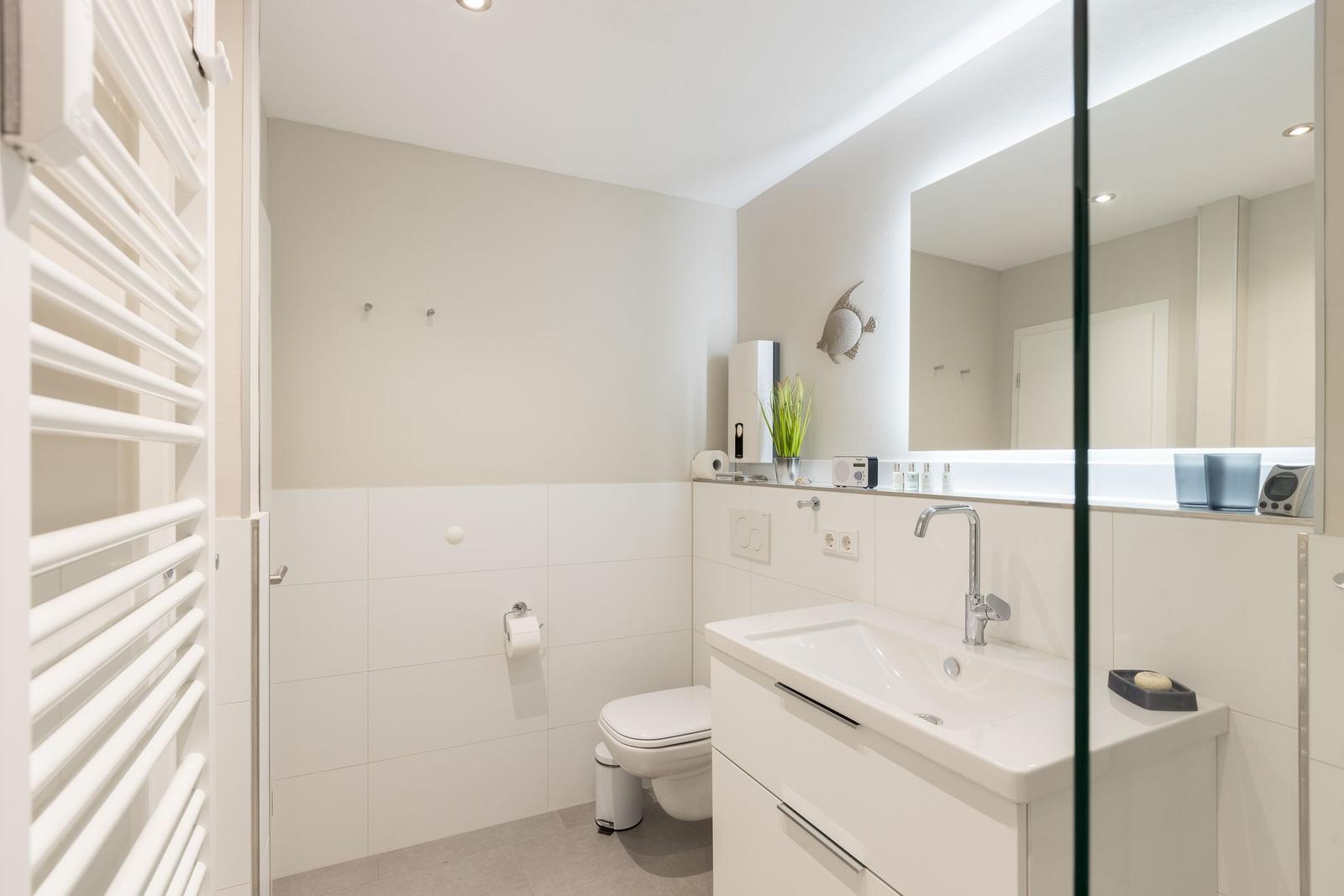 Badezimmer mit Waschbecken, Spiegel, Toilette und Heizkörper.