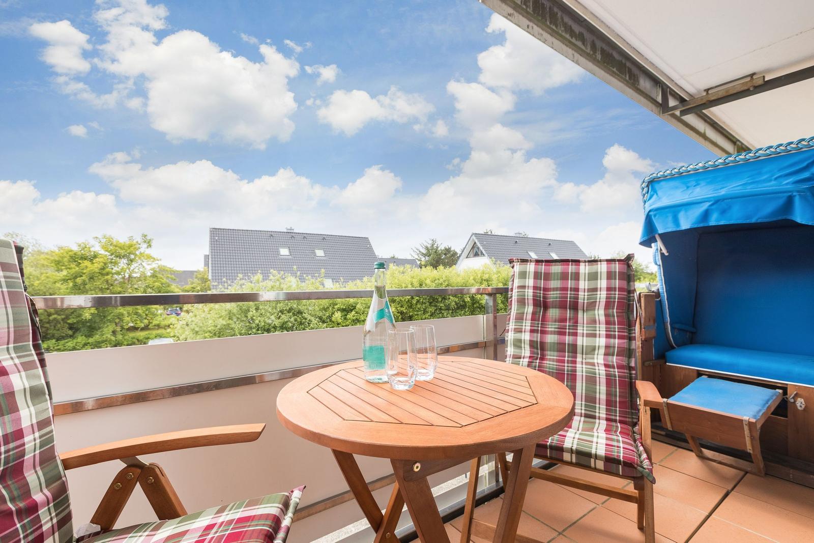 Balkon mit Tisch, Stühlen und Blick auf Häuser und Bäume.