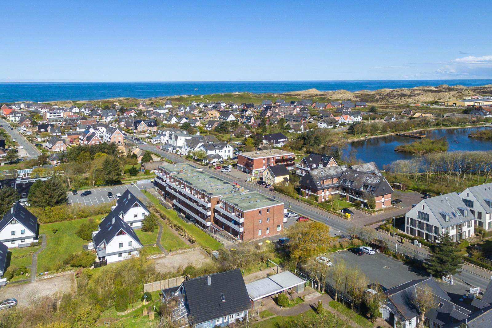 Überblick über ein Dorf mit Häusern, einem See und dem Meer im Hintergrund.