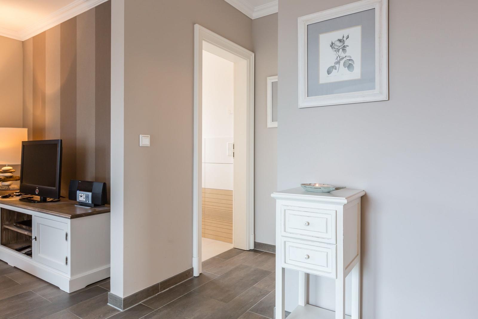 Flur mit weißen Möbeln und Bild an der Wand. Tür führt in Bad.