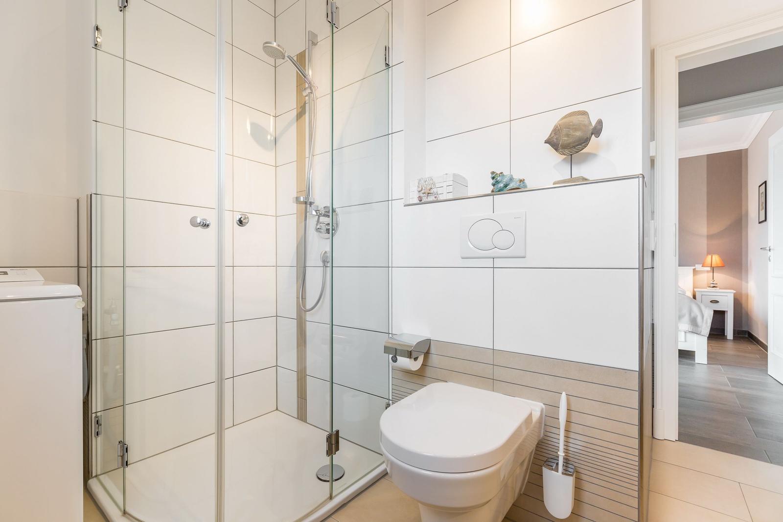 Badezimmer mit Dusche, WC und Waschmaschine. Blick in das Schlafzimmer.