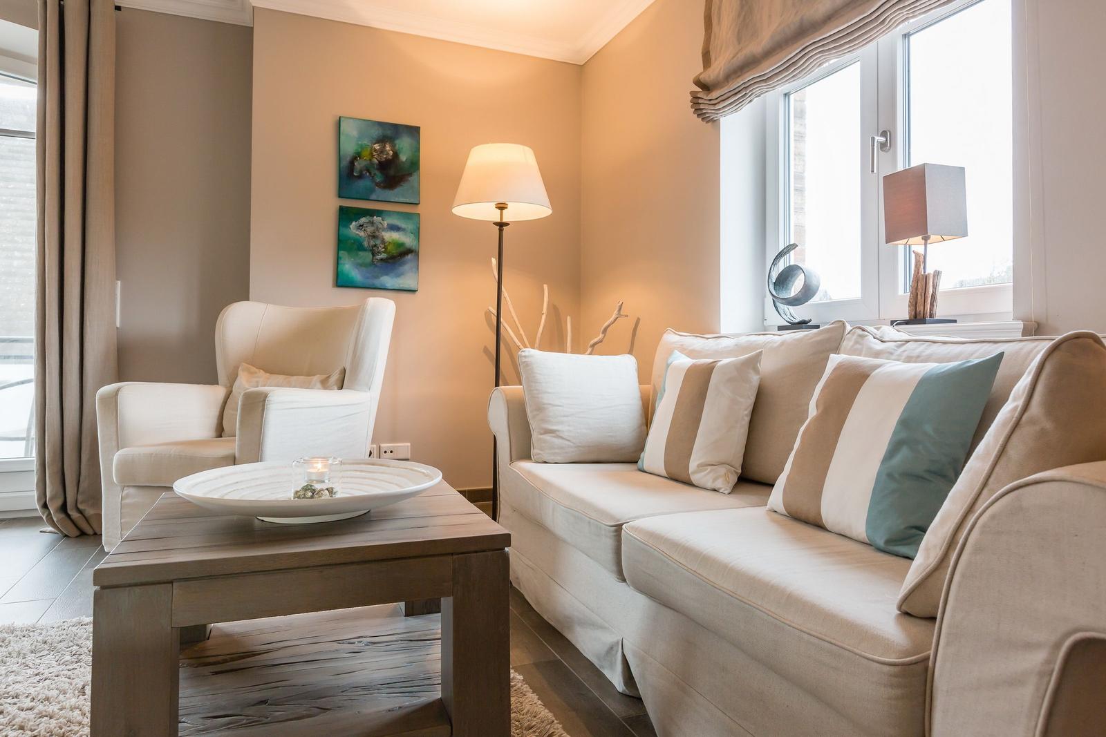 Wohnzimmer mit Sofa, Sessel und Tisch. Wandbilder und Lampen sichtbar.