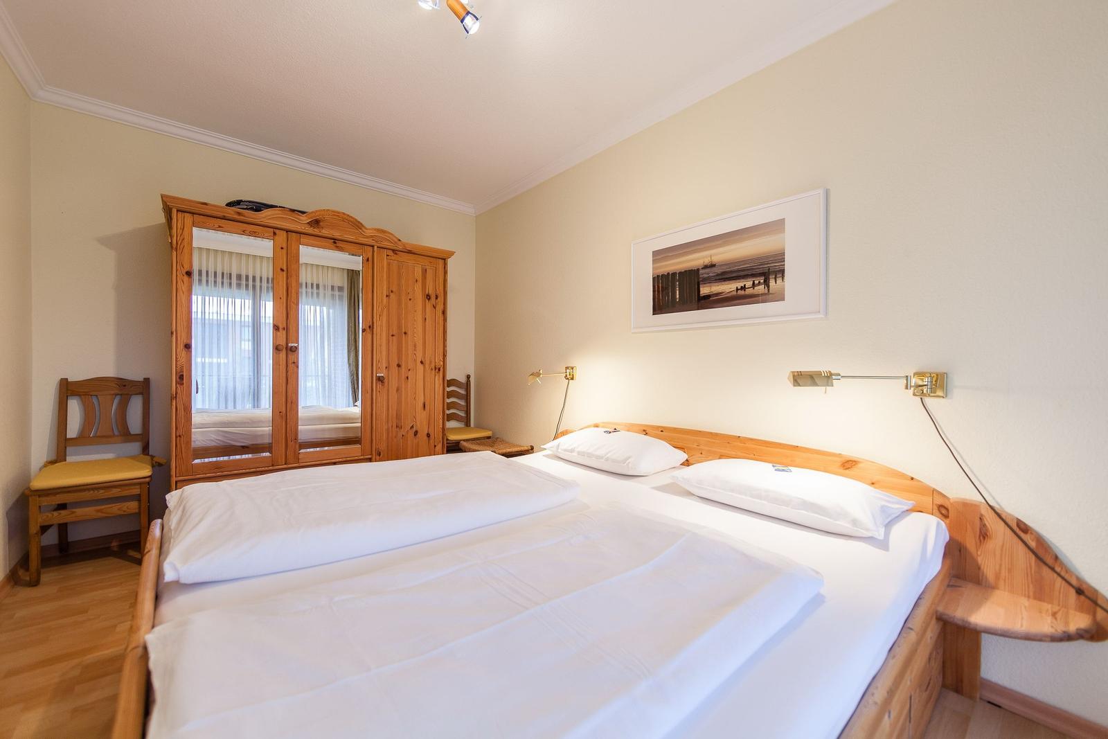 Schlafzimmer mit Holzbett, Kleiderschrank und Wandbild.