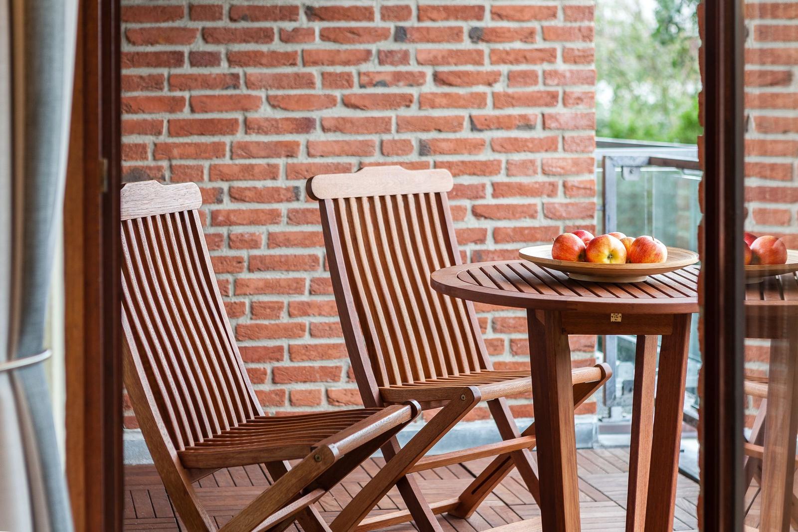Terrasse mit Holztisch und zwei Stühlen. Auf dem Tisch steht eine Schale mit Äpfeln.