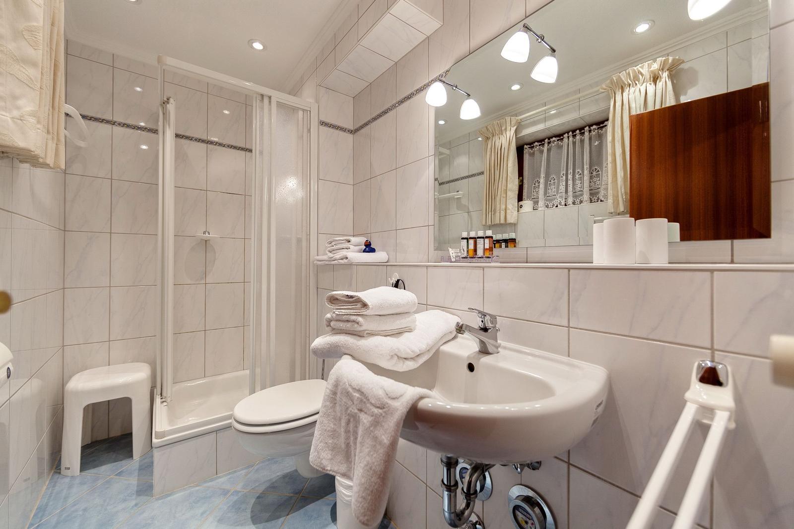 Badezimmer mit Dusche, Waschbecken und Toilette. Weiße Fliesen und Handtücher.