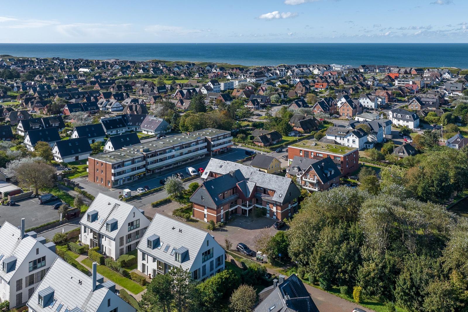 Aerial view of a coastal town with houses and greenery near the sea.