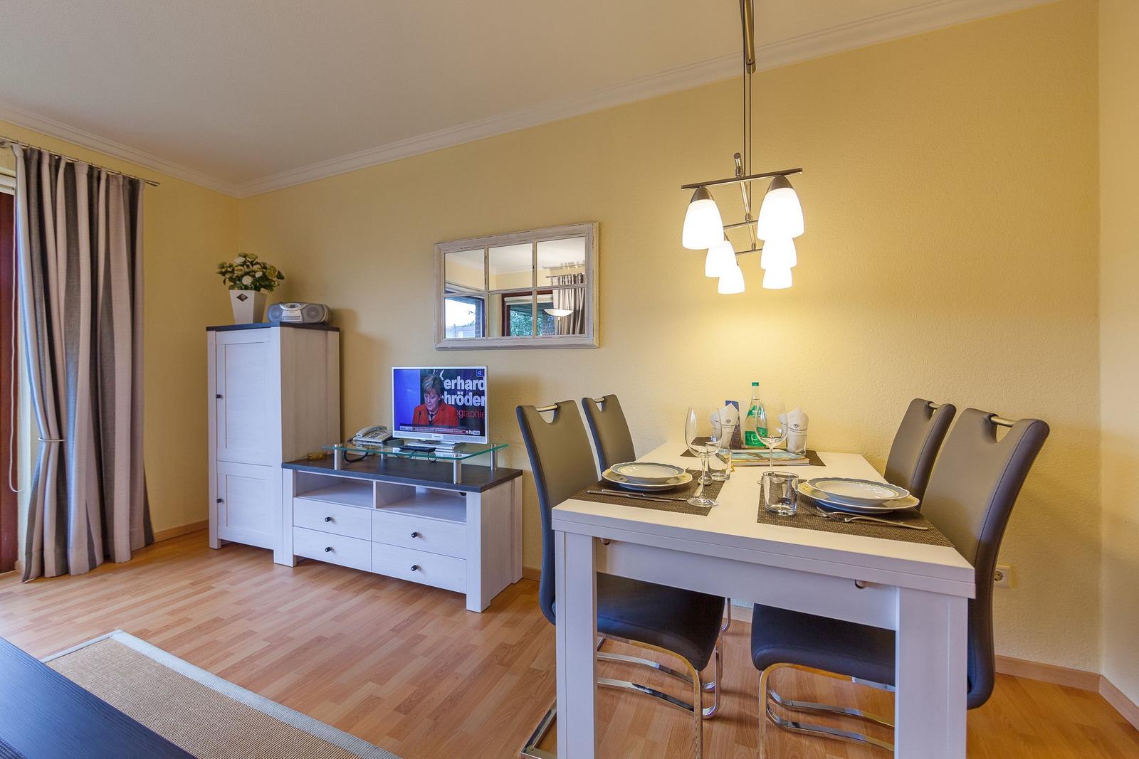 Esszimmer mit Tisch, Stühlen und Fernseher. Helle Wandfarbe und Holzboden.