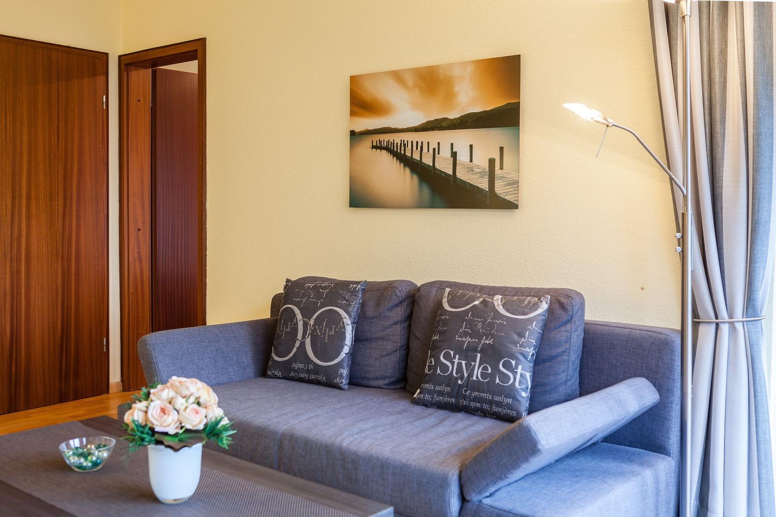 Ein grauer Sofa mit Kissen, Wandbild und Stehlampe im Wohnzimmer.
