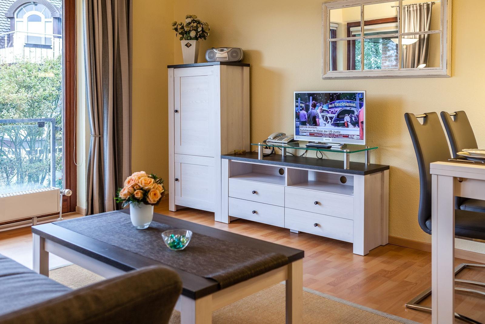 Wohnzimmer mit TV, Tisch, Stühlen und Fenster zum Balkon.