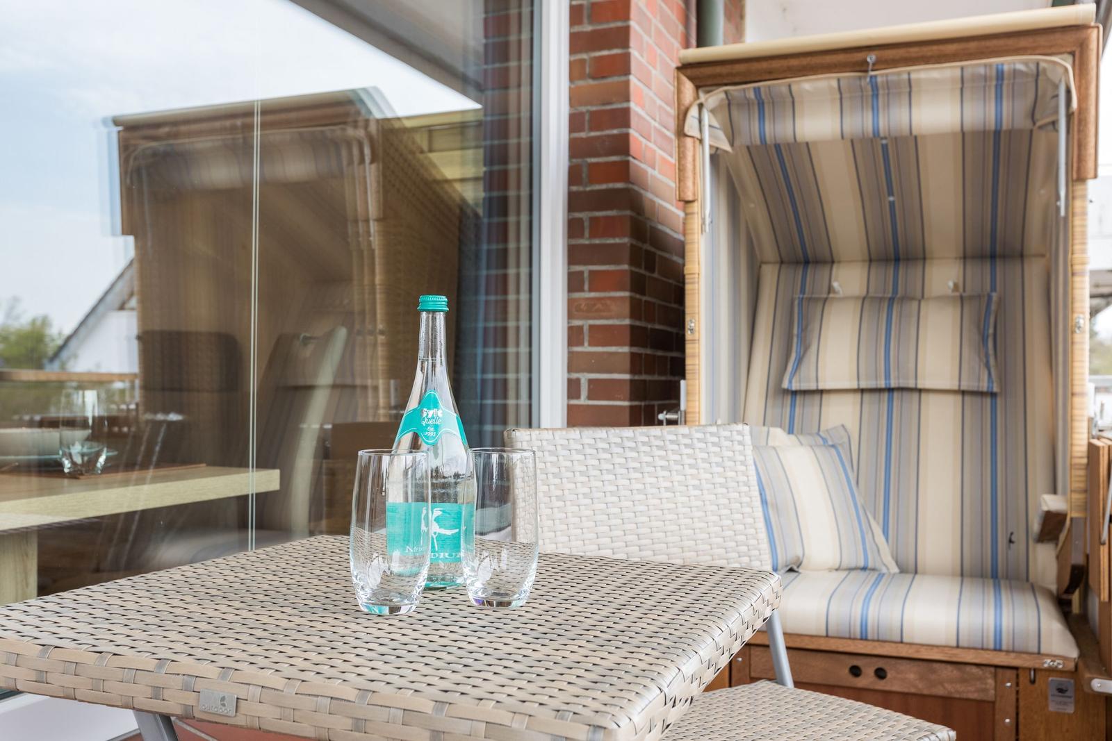 Terrace with table, chairs, and lounge. On the table is a water bottle and two glasses.