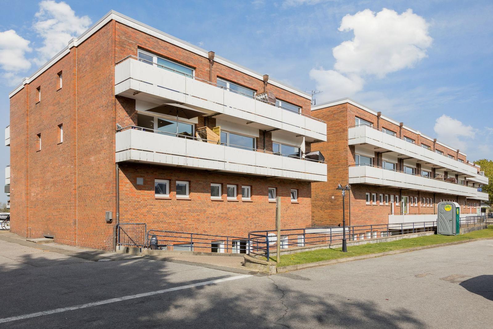 Red brick building with balconies and windows under blue sky.