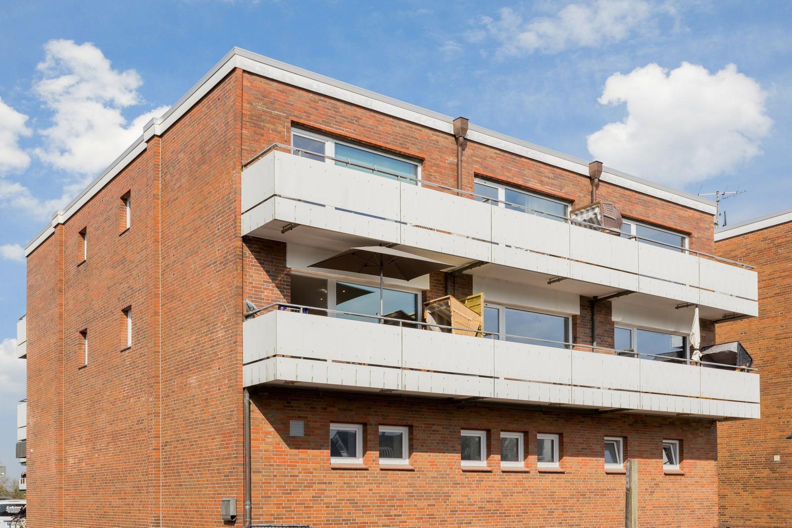 Two-story apartment building with balconies and red brick facade under blue sky.