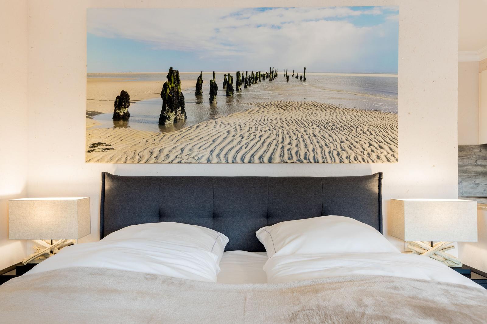 Bedroom with bed and wall art of beach and posts.