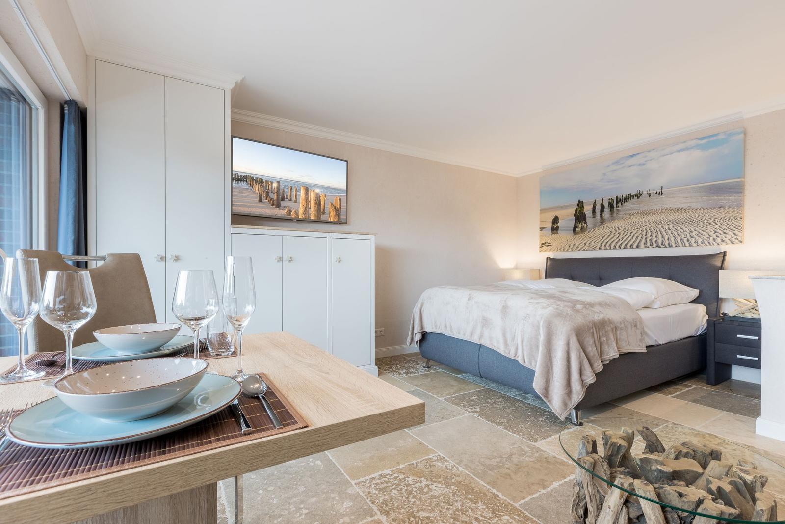 Bedroom with bed, table, and wall art. TV and cabinet are visible.