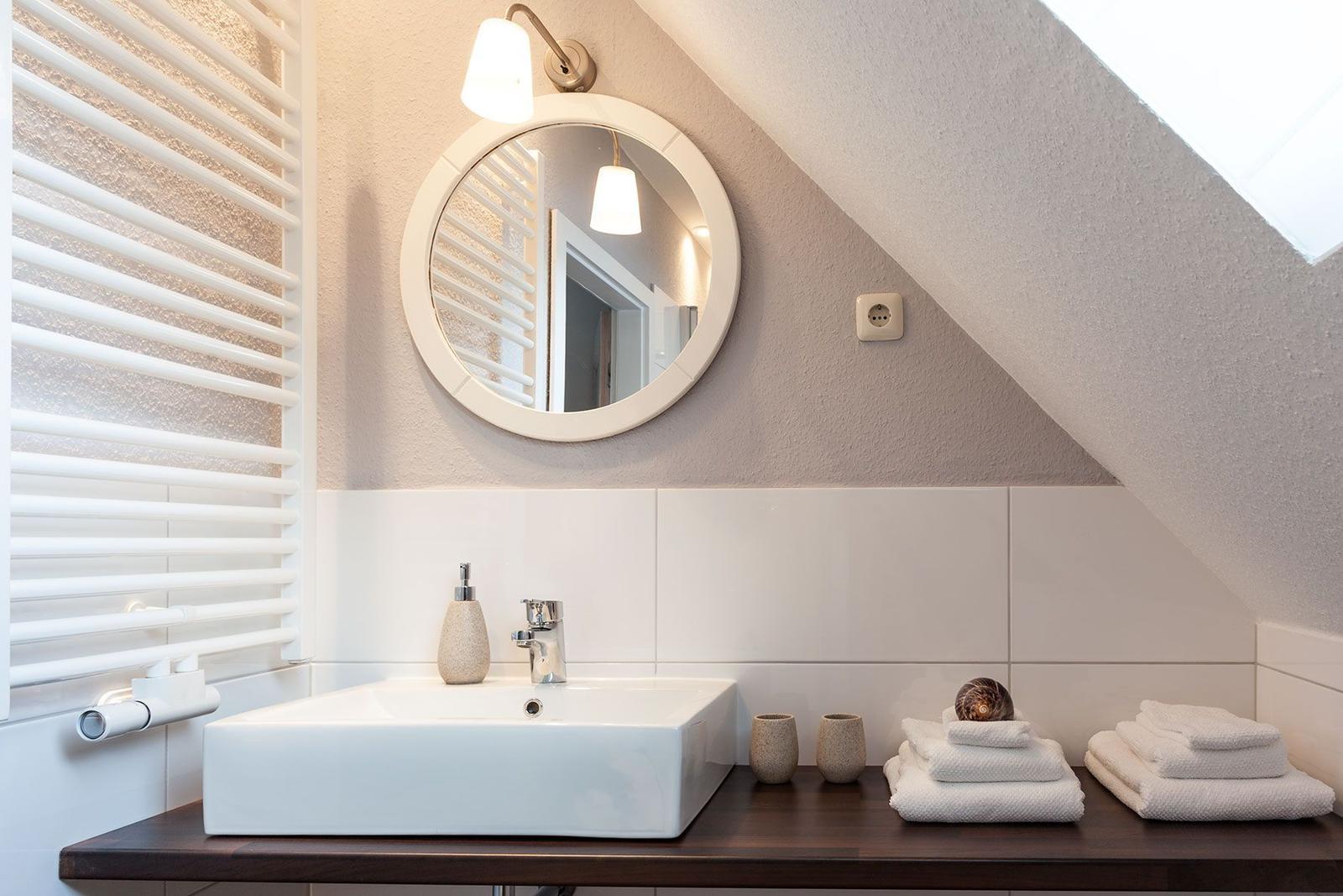 Dusche mit Waschbecken, Spiegel und Handtüchern unter Dachschrägen.