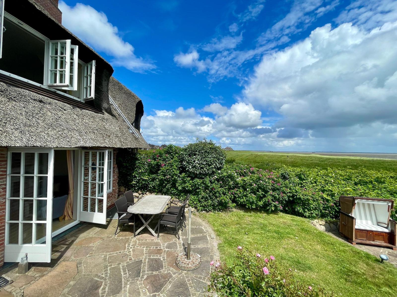 Haus mit Dachstuhl, Terrasse, Tisch, Stühle und Blick auf grüne Wiesen.