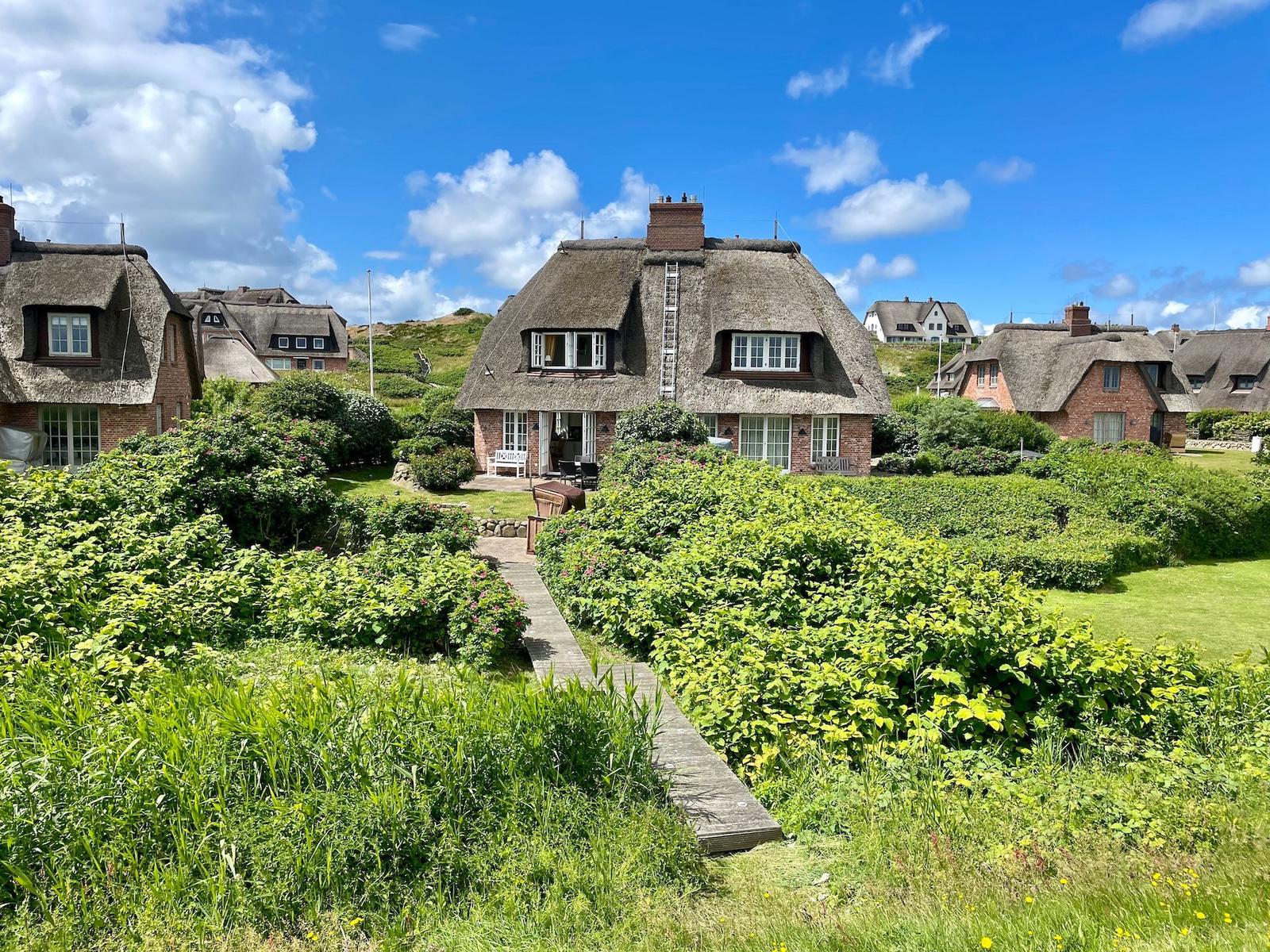 Dorfhaus mit Strohdach und Gartenweg unter blauem Himmel.