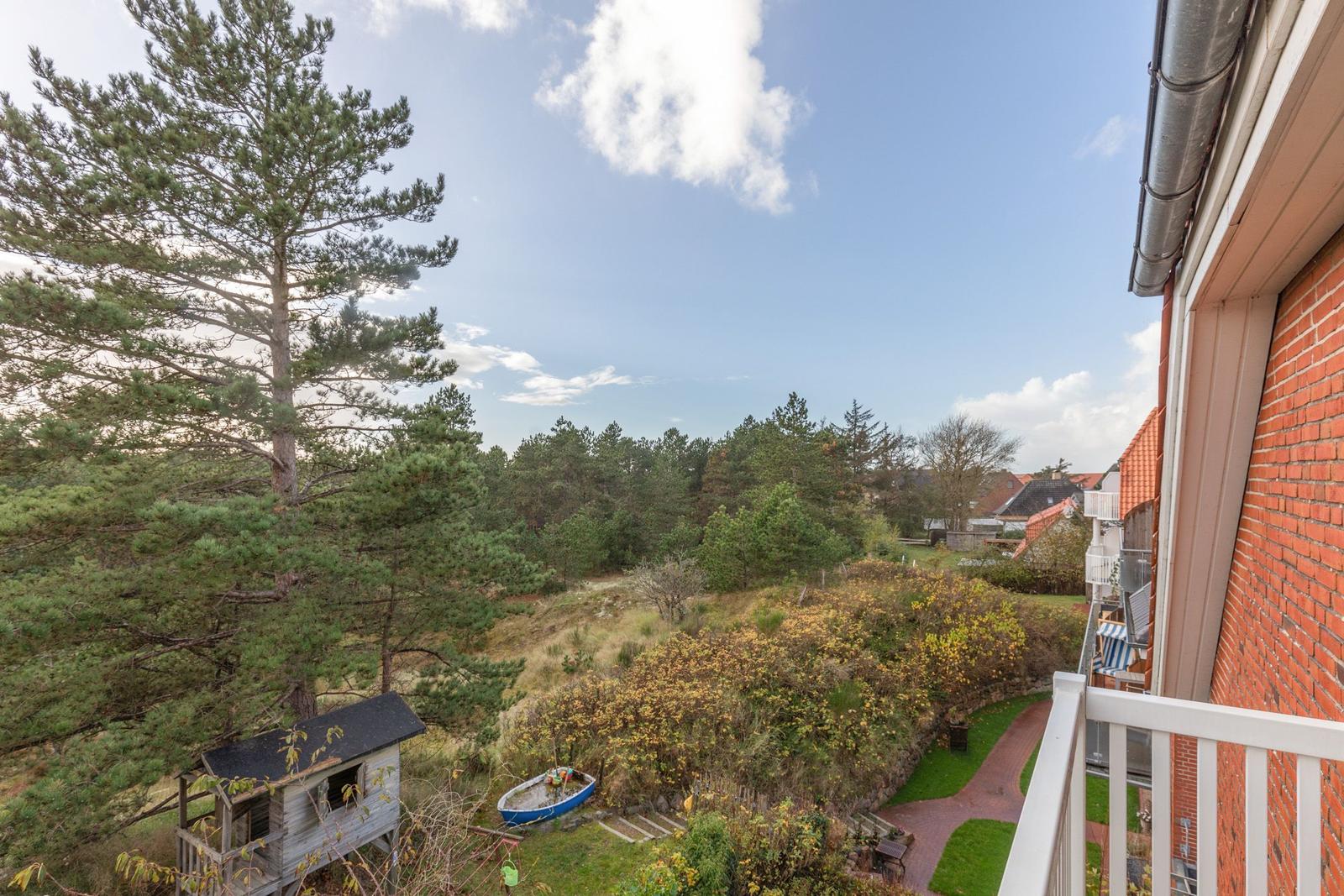 Blick von Balkon auf Grünfläche, Baum, kleine Hütte und Boot.