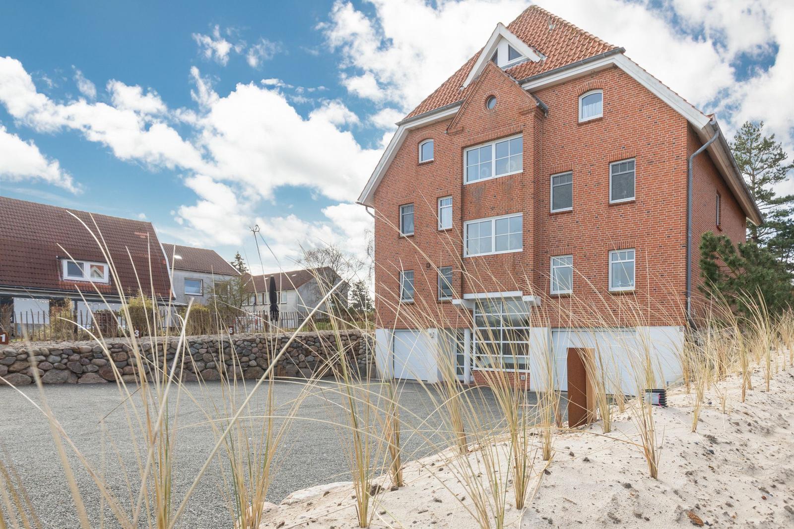 Rotes Backsteinhaus mit Dachgauben und Garagen. Vordergrund: Sand und Gräser.
