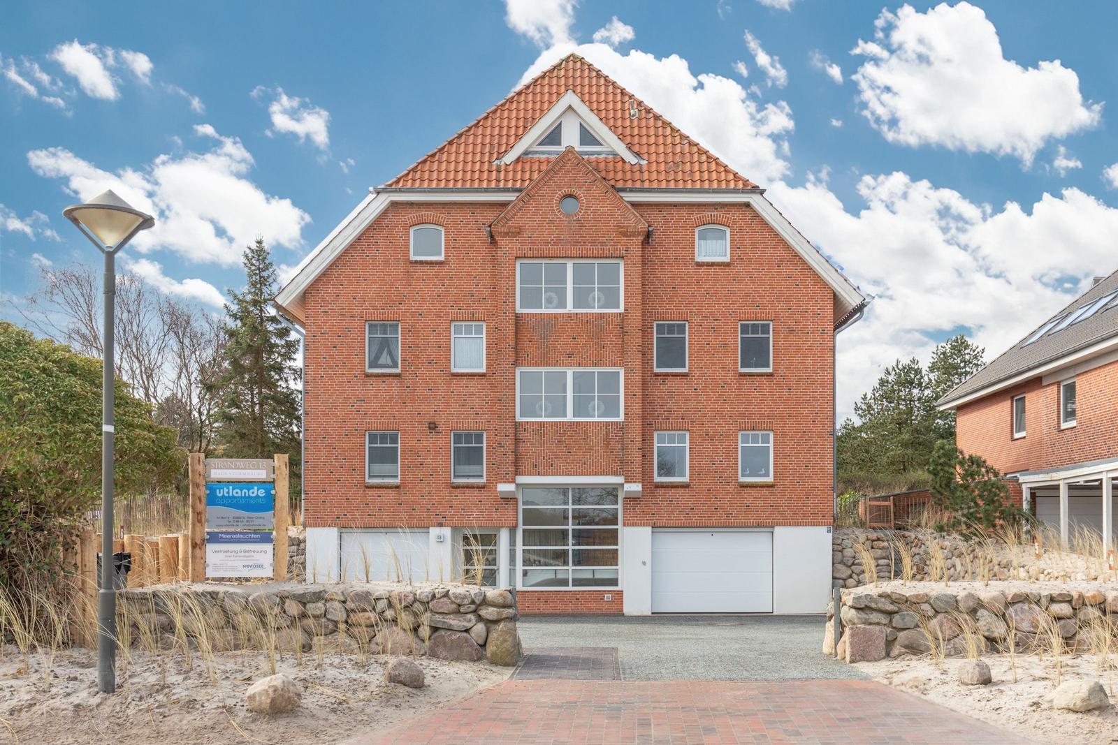 Rotes Backsteingebäude mit Garage und Dachgauben unter blauem Himmel.