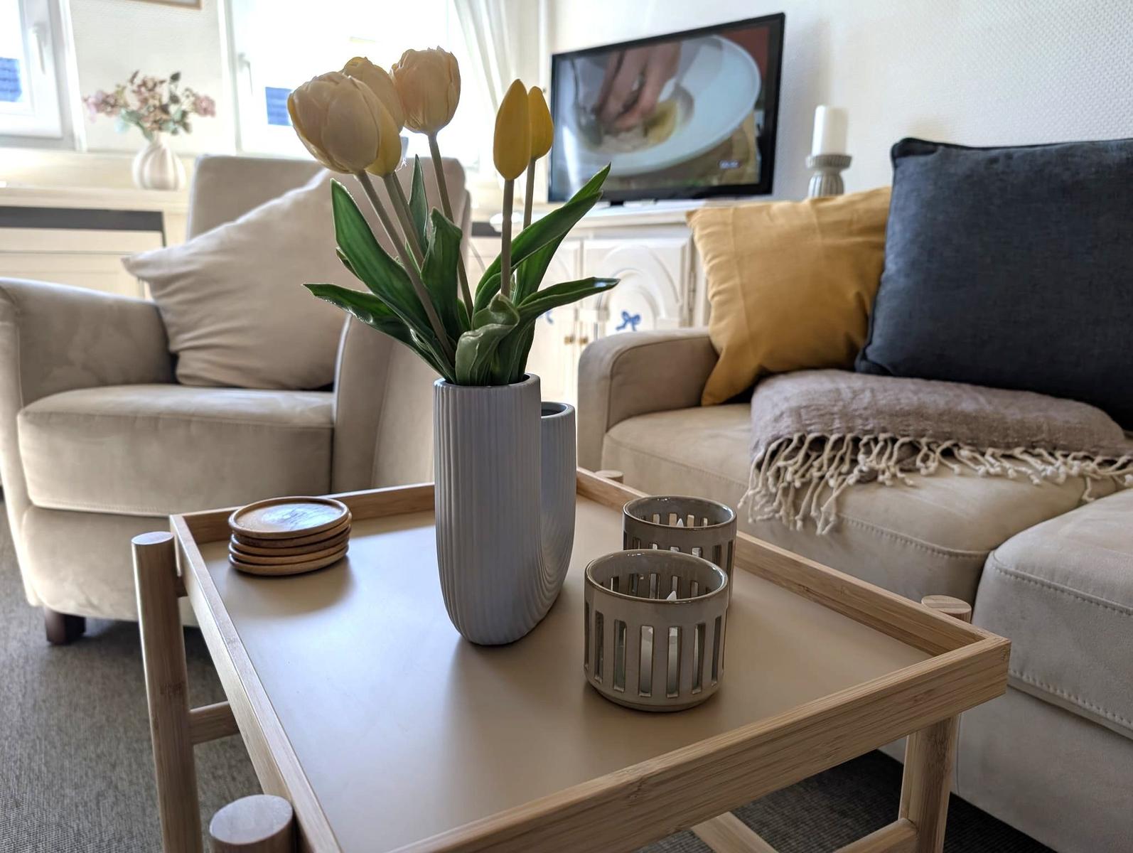 Wohnzimmer mit Couch, Tisch und Blumen.