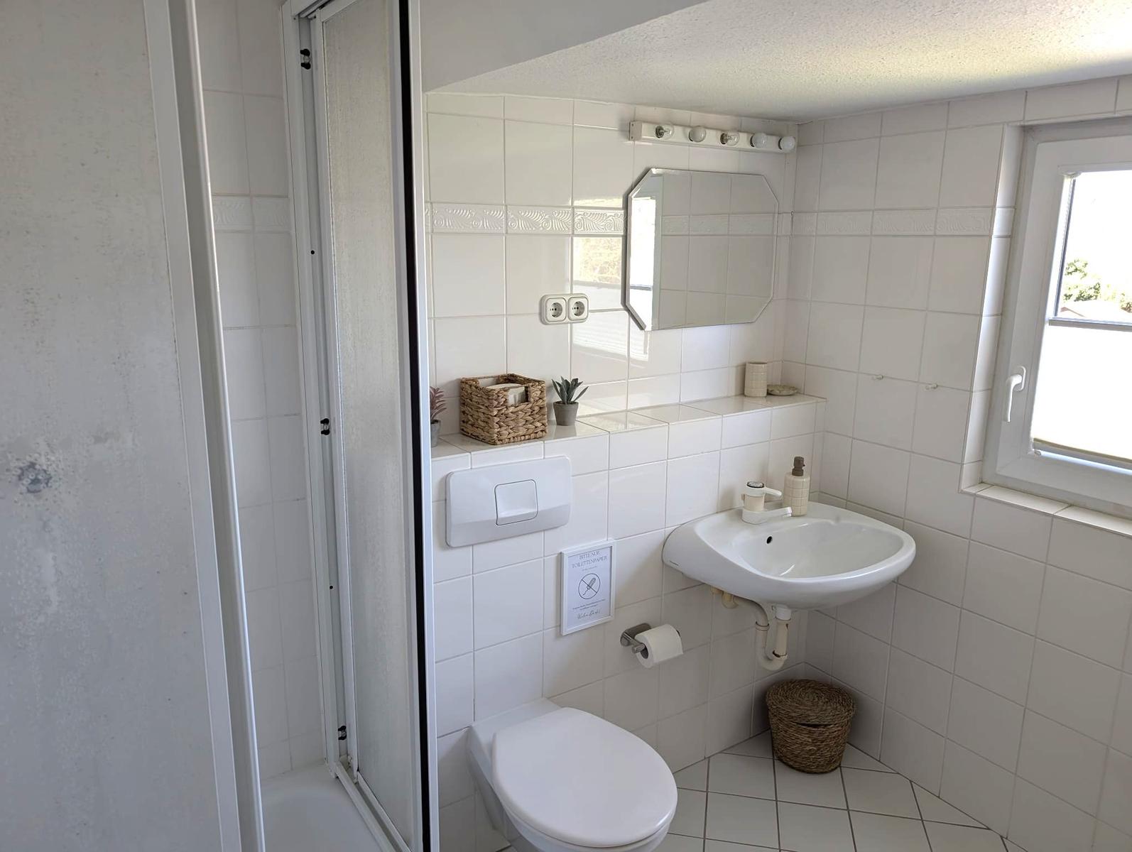 Badezimmer mit Dusche, Waschbecken und Toilette. Weiße Fliesen und Spiegelschrank.