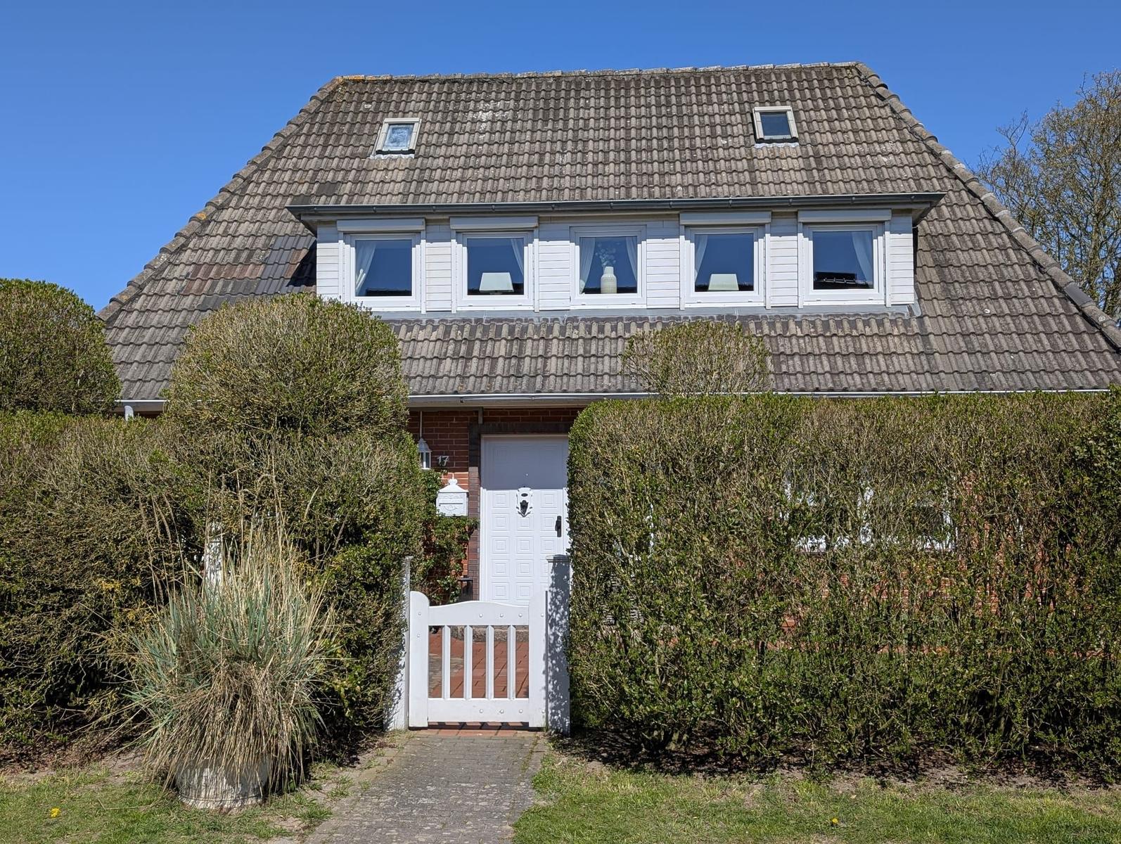 Haus mit Dachfenstern, weißer Tür und Hecke