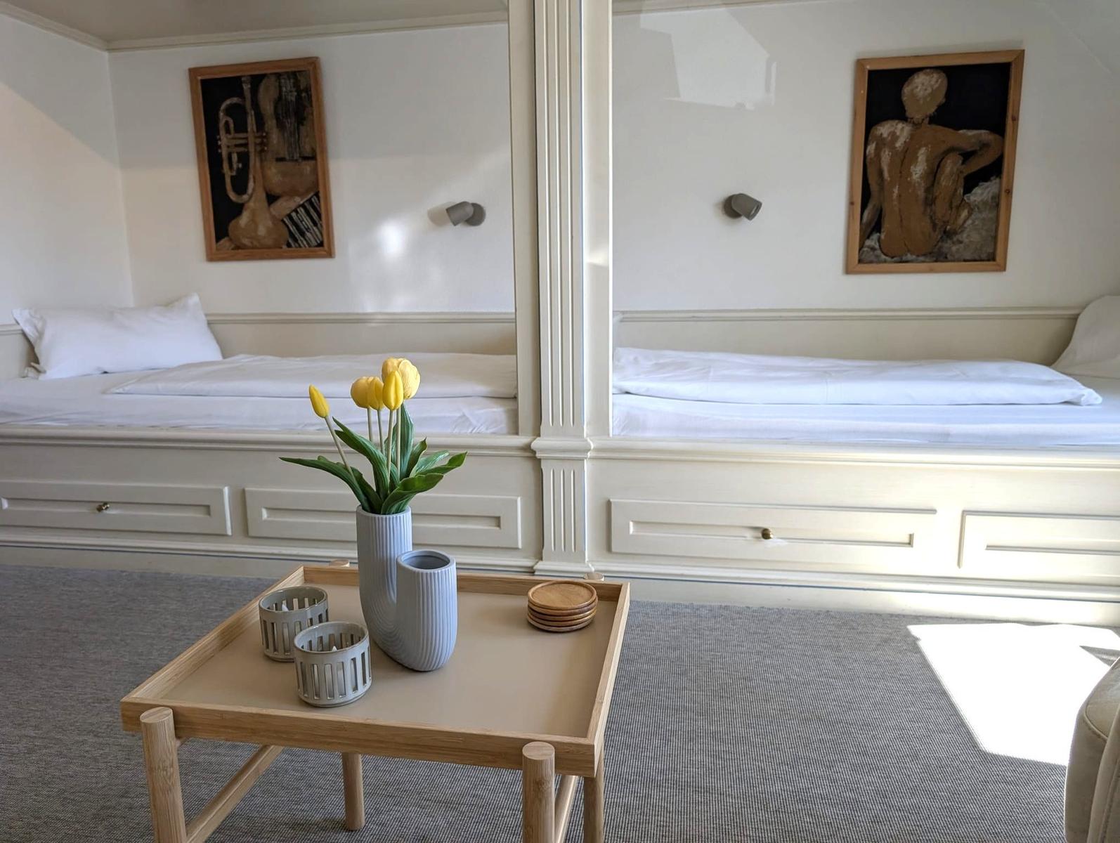 Zwei Betten mit weißen Laken, Tisch mit Tulpen und Wandbildern.