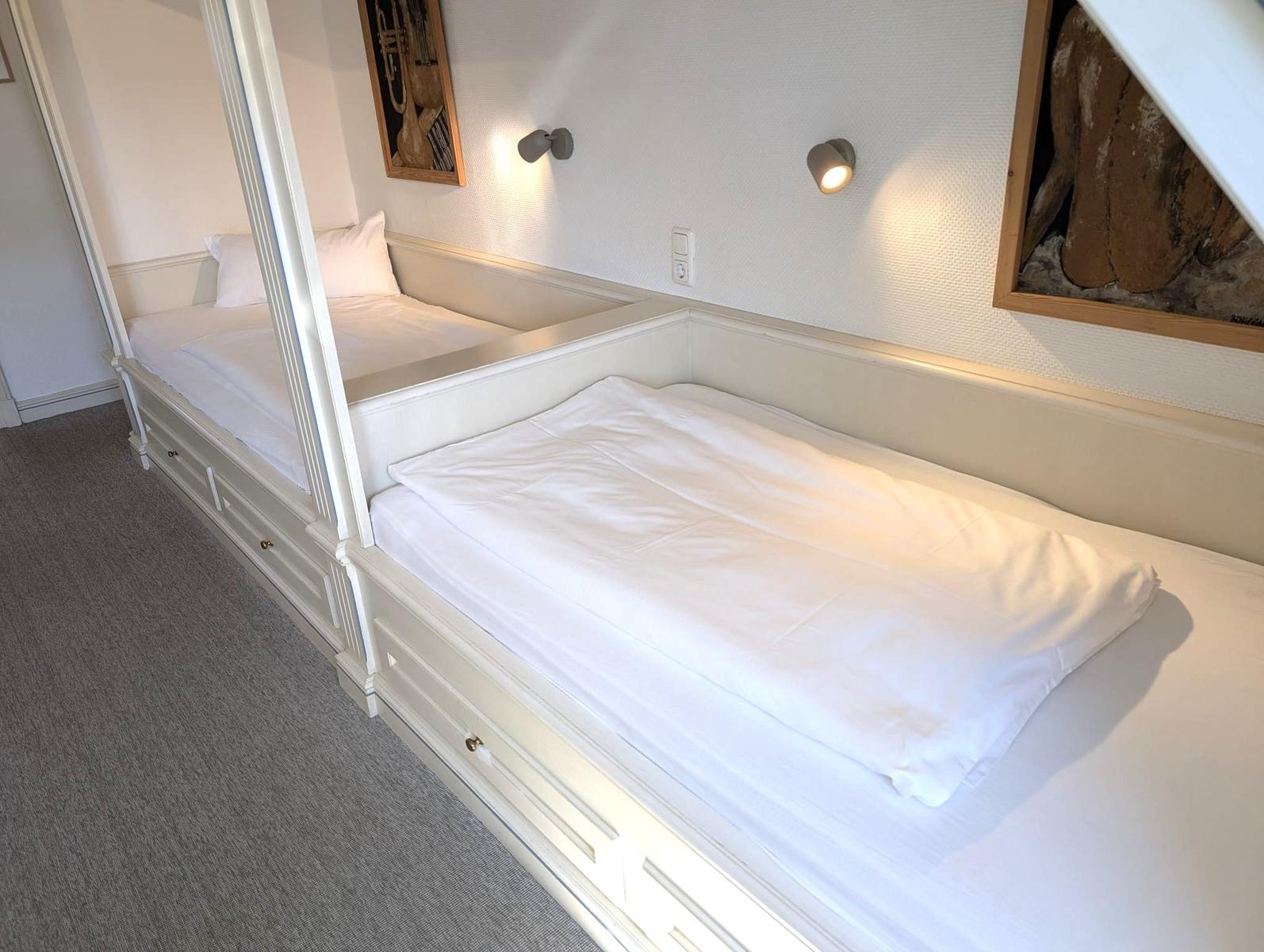 Zwei Betten mit weißen Bettwäschen und Wandlampen an der Wand.