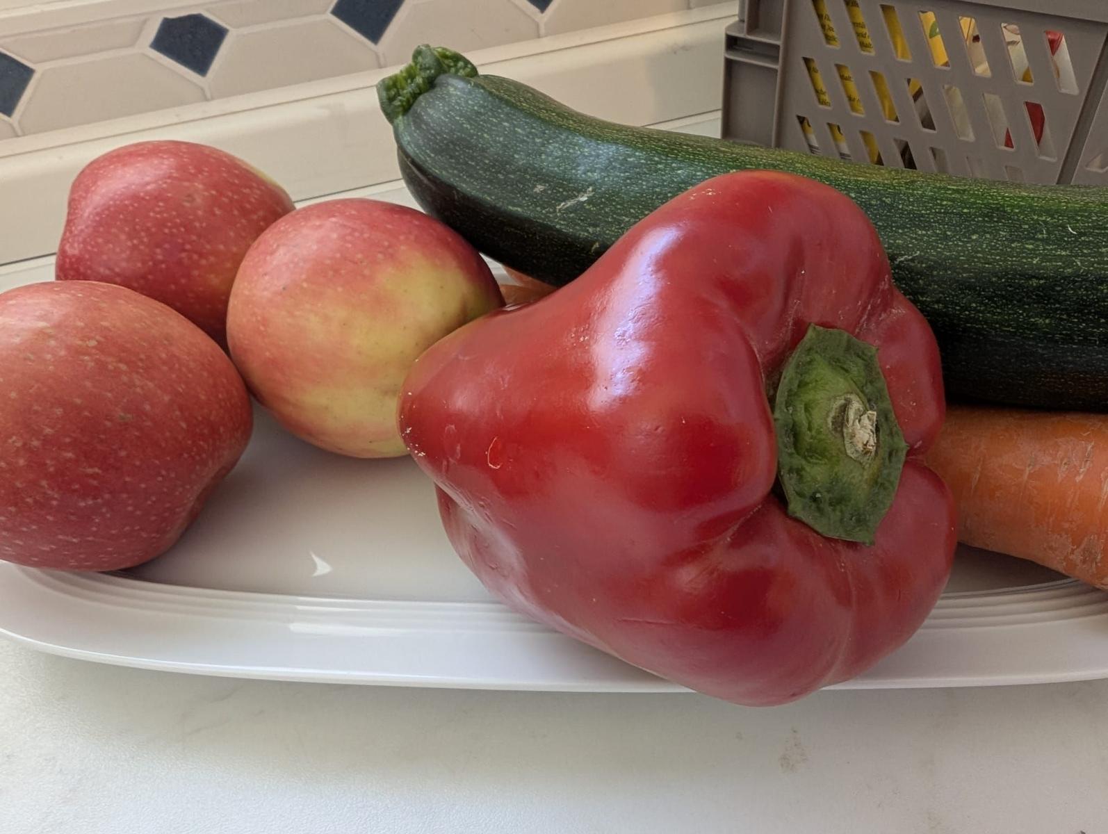 Auf einem Teller liegen Äpfel, eine Paprika, eine Zucchini und eine Karotte.