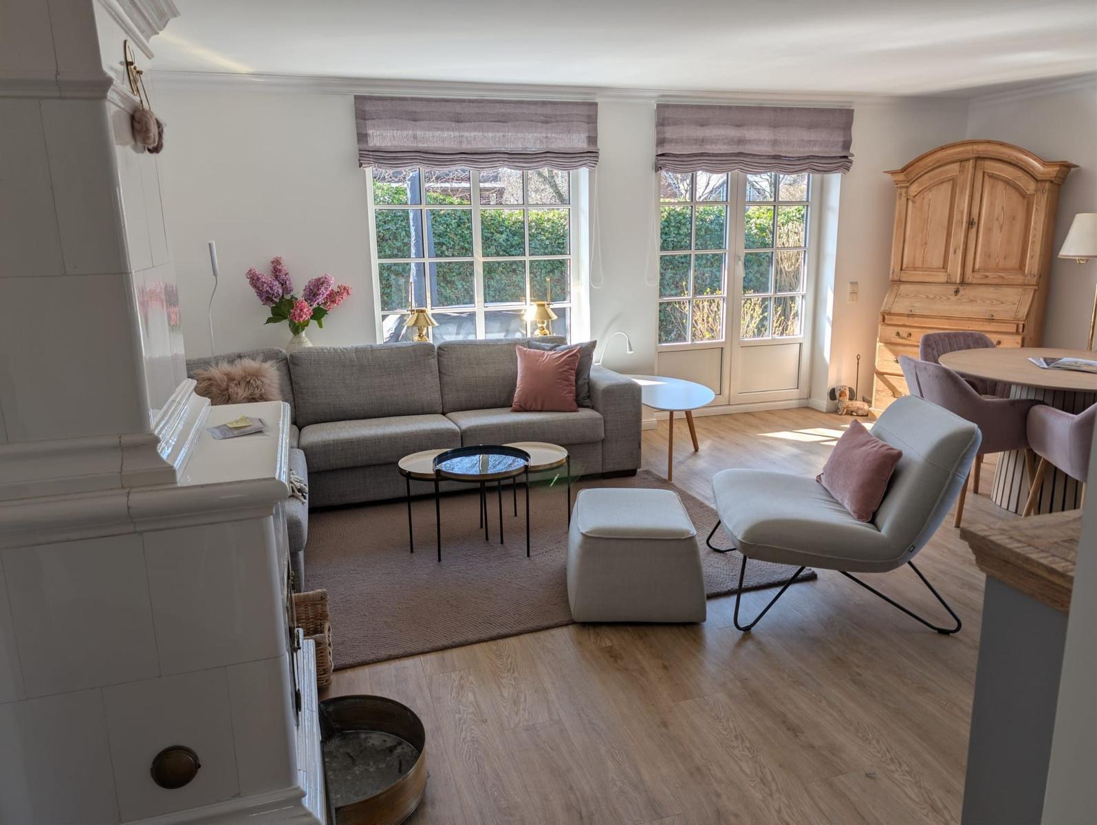Living room with sofa, armchair, and dining table. Wooden floor and large windows.