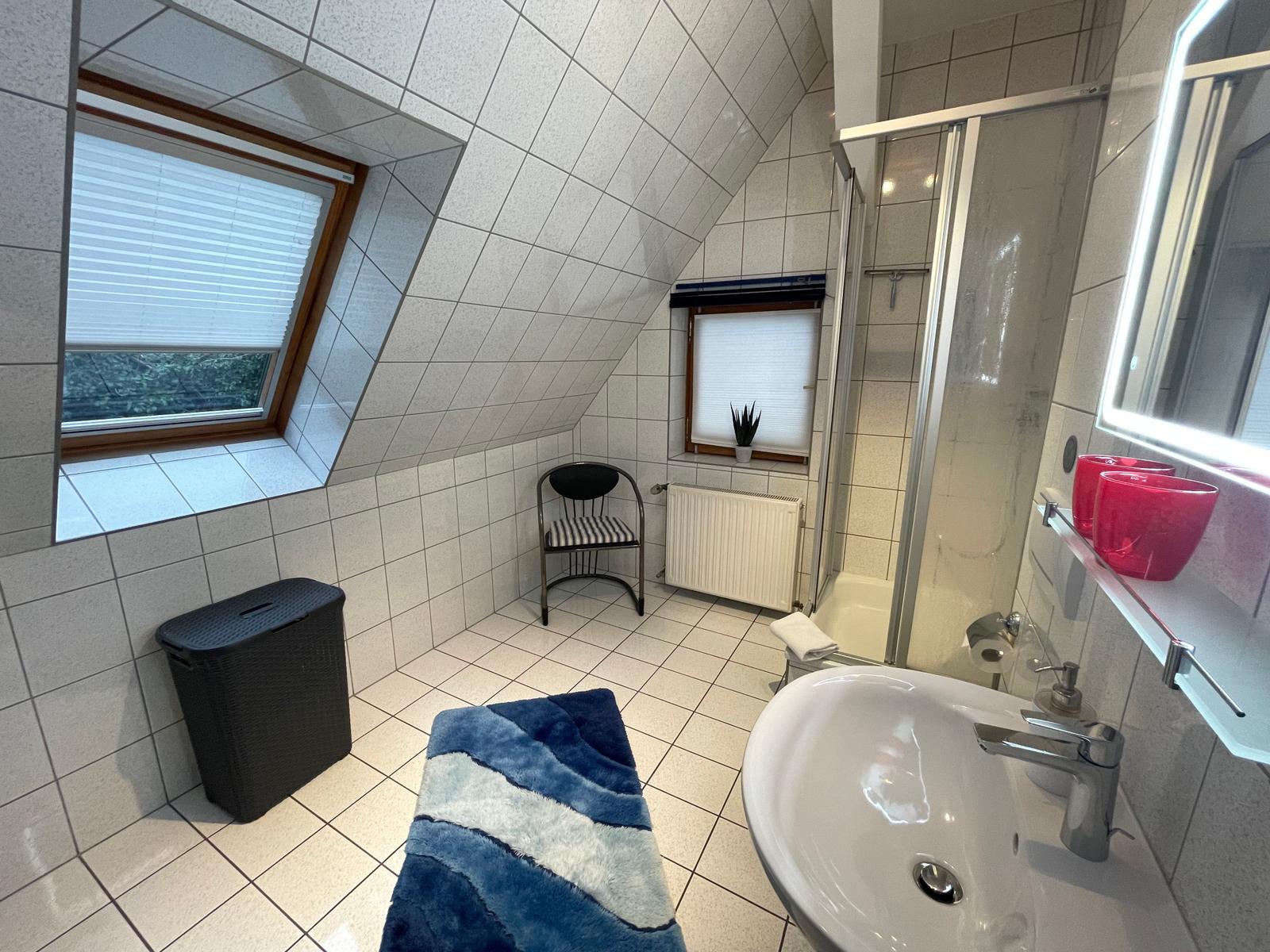 Helles Bad mit Dachfenster, Toilette, Dusche und großes Waschbecken mit beleuchtetem Spiegel.
