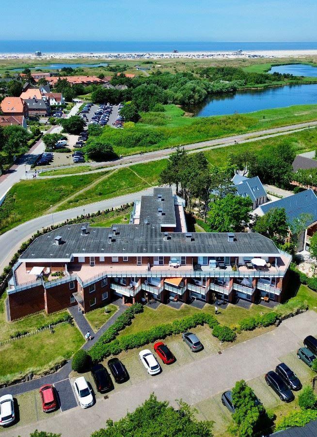 Modernes Mehrfamilienhaus mit Balkonen und Parkplatz. Grünanlagen und Wasser im Hintergrund.