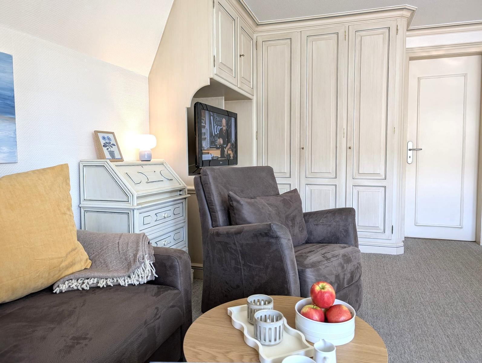 Wohnzimmer mit Sofa, Sessel, Fernseher und Schreibtisch.