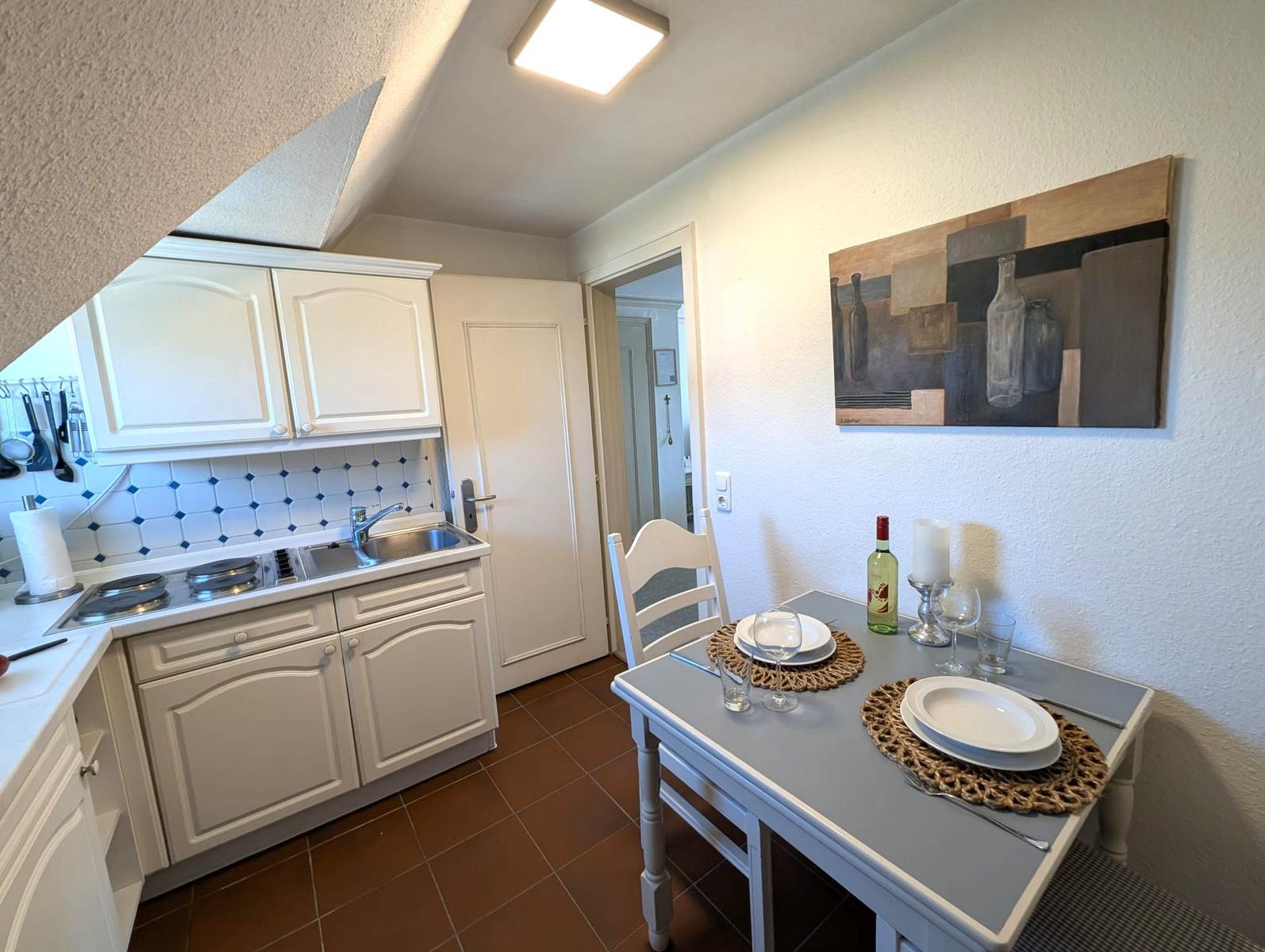 Küche mit Essbereich, weißer Arbeitsplatte und Holztisch mit Stühlen.