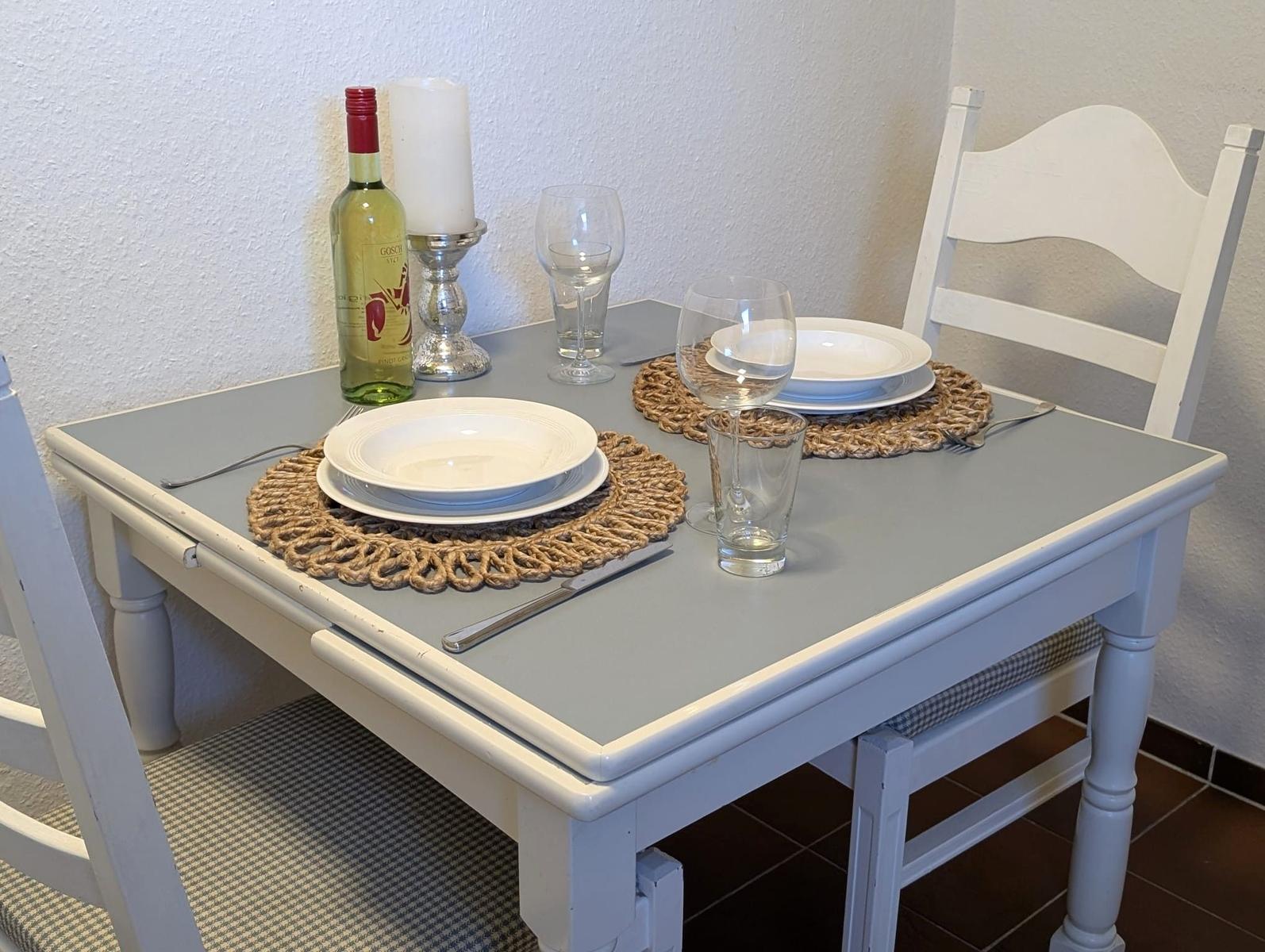 Esstisch mit zwei Plätzen, Tischdecken, Gläser und Flasche.