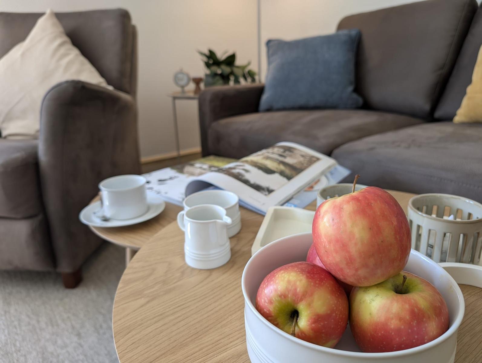 Tisch mit Äpfeln, Tassen und Zeitschriften vor einem Sofa