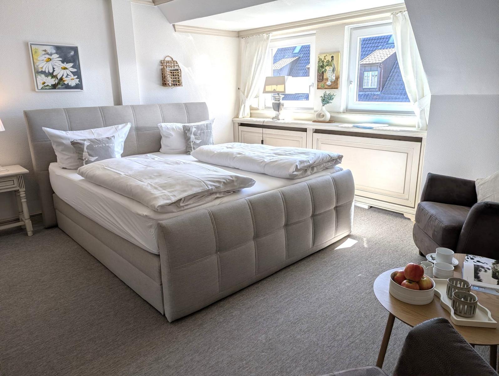 Schlafzimmer mit Doppelbett, Fenster und Sitzgelegenheit.