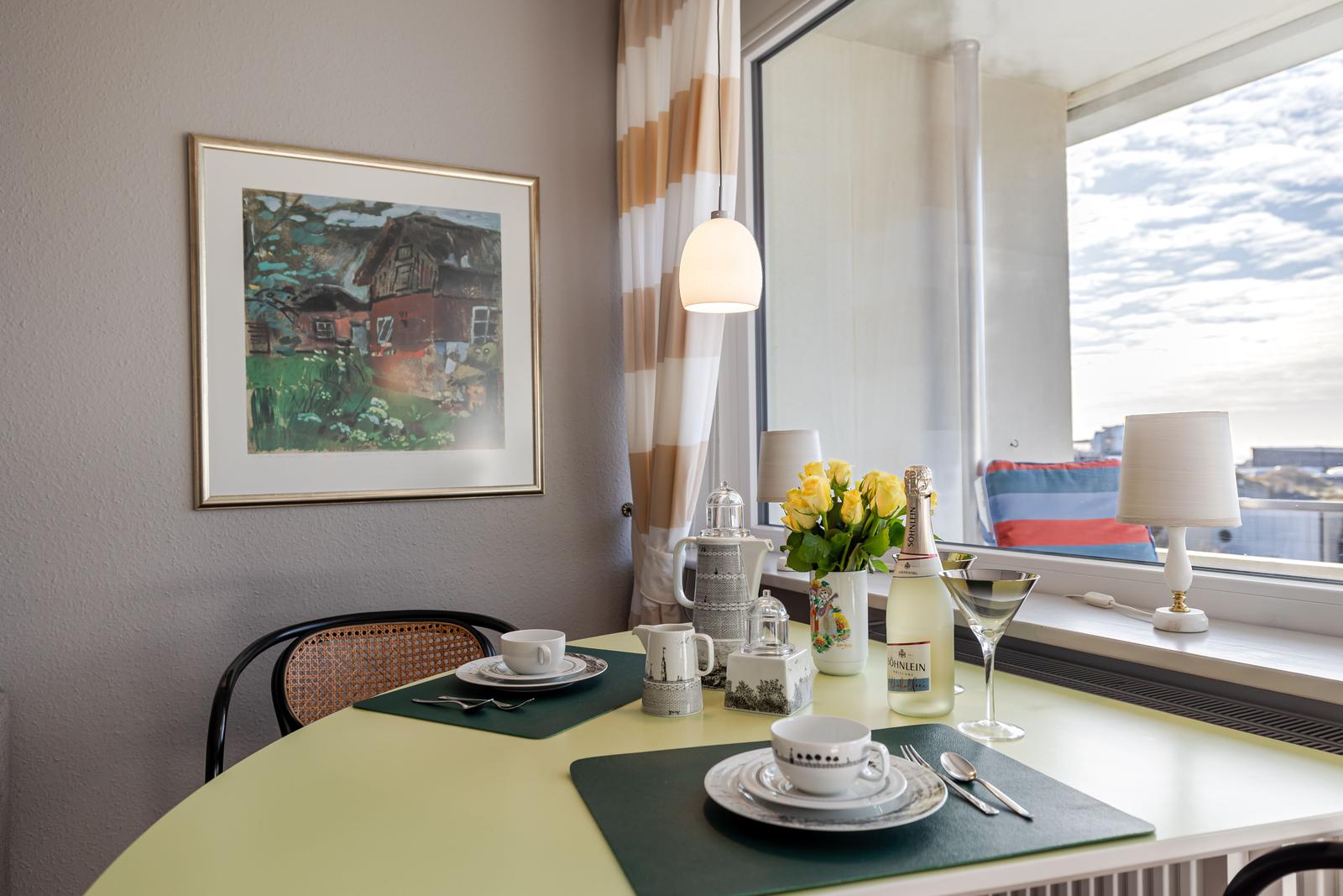 Tisch mit Geschirr, Blumen und Flasche vor Fenster mit Blick.