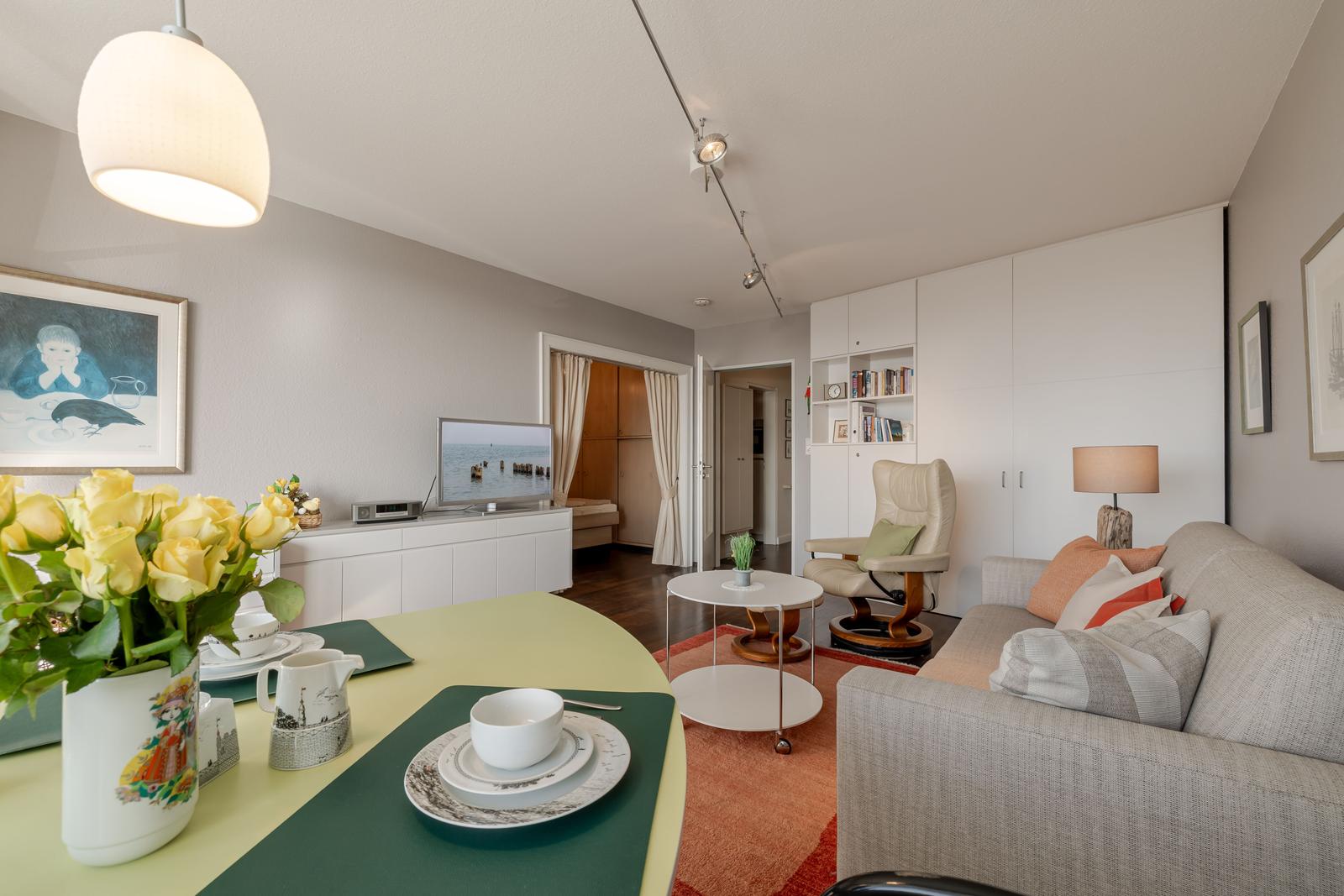 Wohnzimmer mit Sofa, Esstisch und Fernseher. Helle Wandfarbe und moderne Einrichtung.