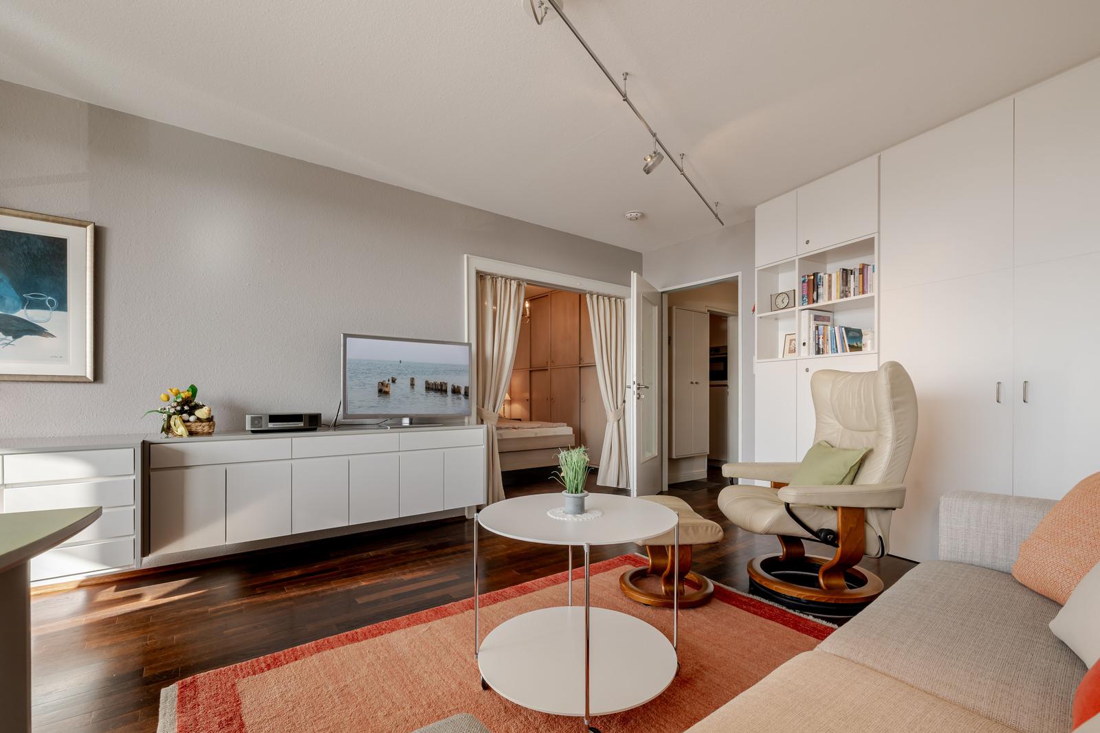 Wohnzimmer mit Sofa, Sessel, Couchtisch und Fernseher.