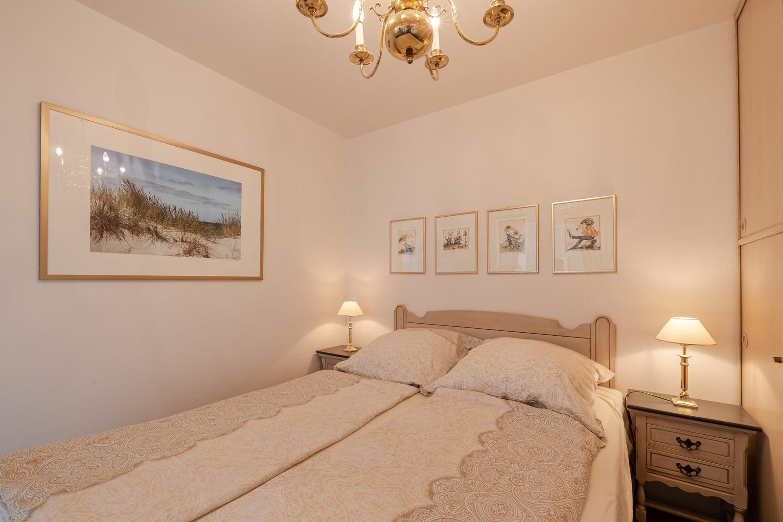Schlafzimmer mit Bett, Nachttischen und Wandbildern.