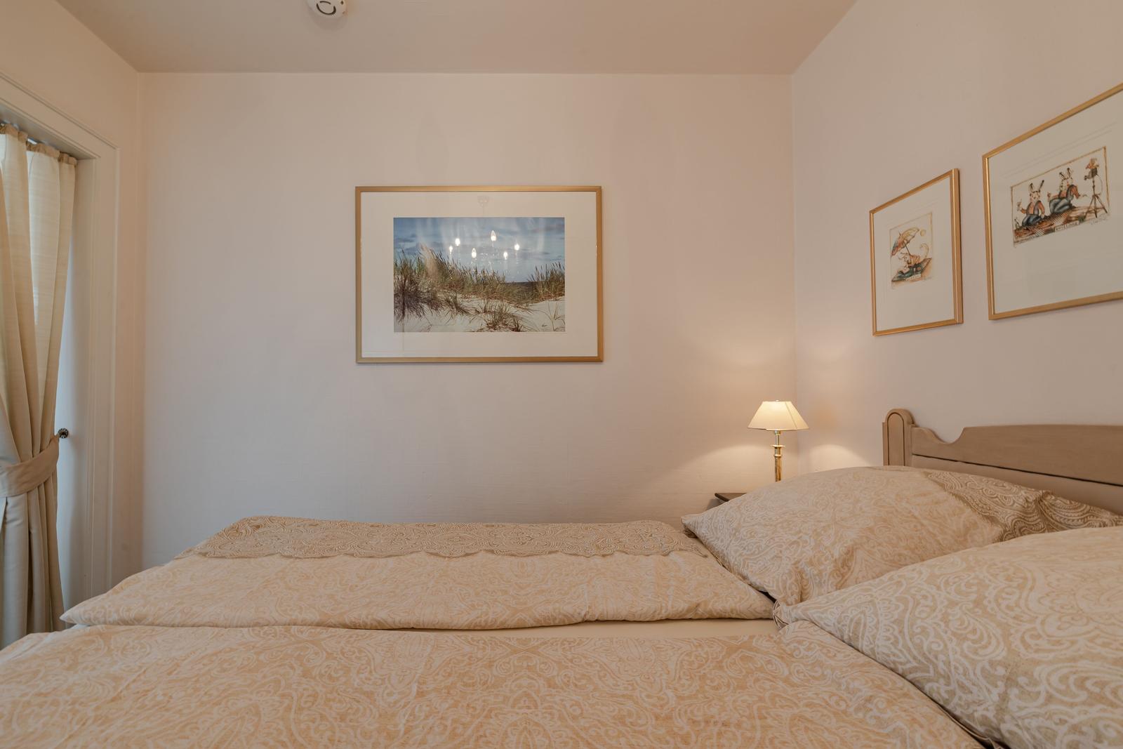 Schlafzimmer mit Bett, Wandbildern und Nachttischlampe.