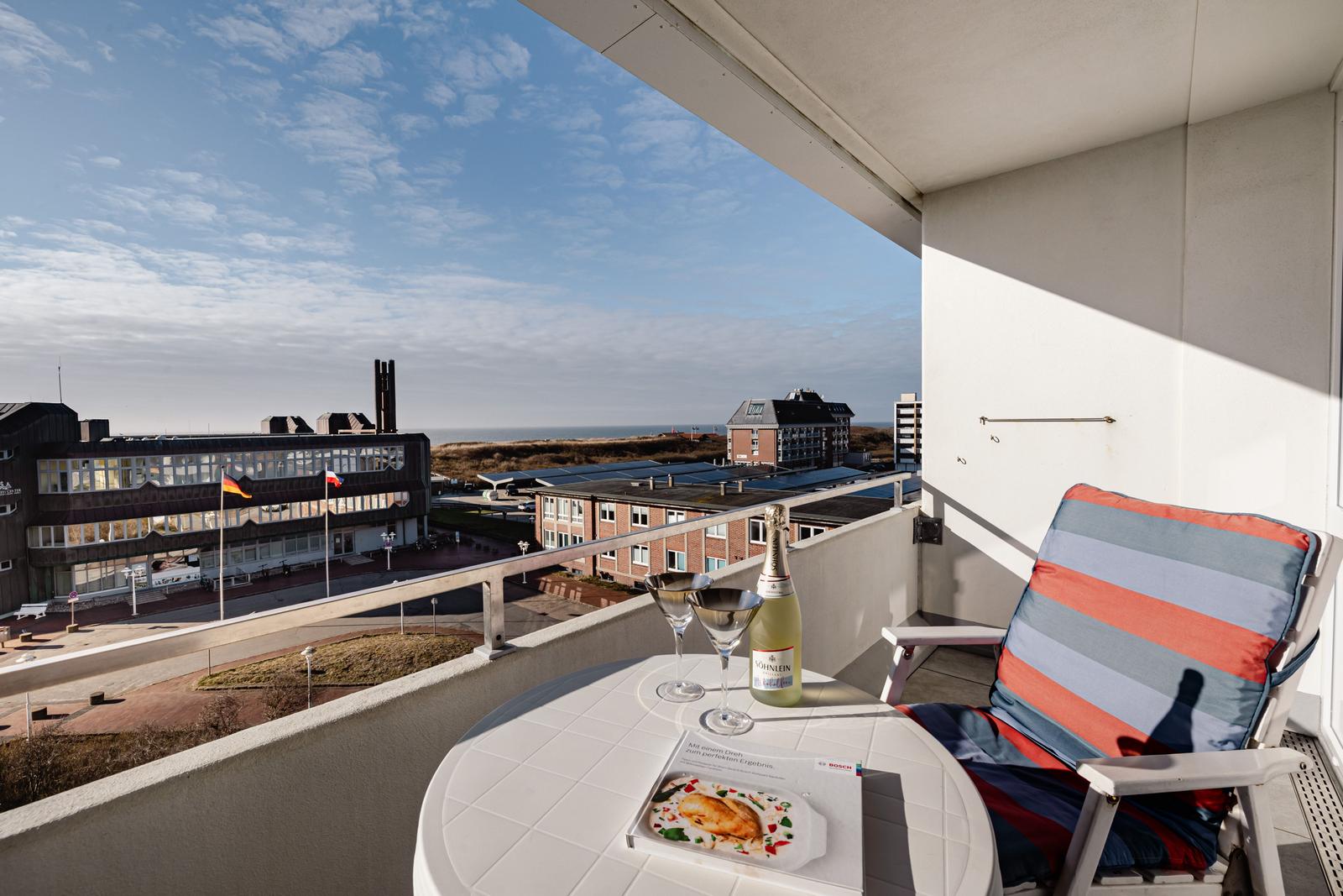Balkon mit Tisch, Stuhl und Seeblick auf Gebäude und Strand.