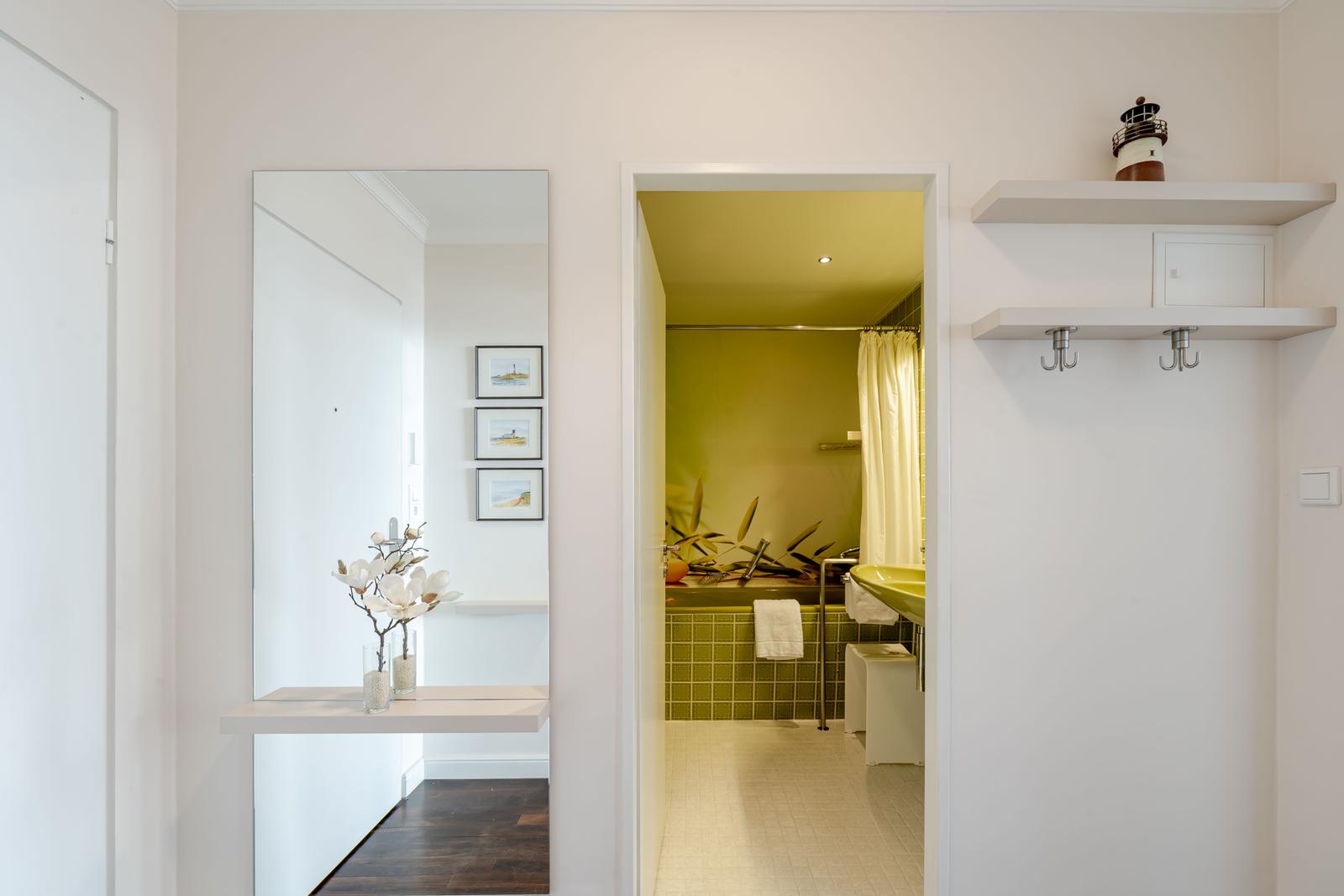 Badezimmer mit grünem Fliesenbereich und Dusche. Flur mit Spiegel und Vase.