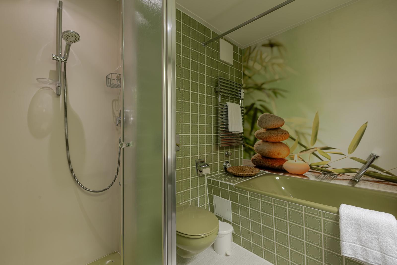 Bad mit Dusche, Toilette und Badewanne mit Steinpyramide und Kerze.