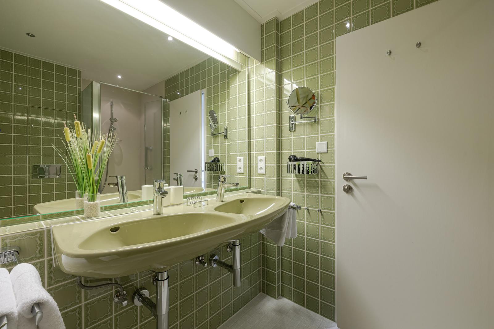 Badezimmer mit grünen Fliesen, Doppelwaschbecken und Spiegelschrank.