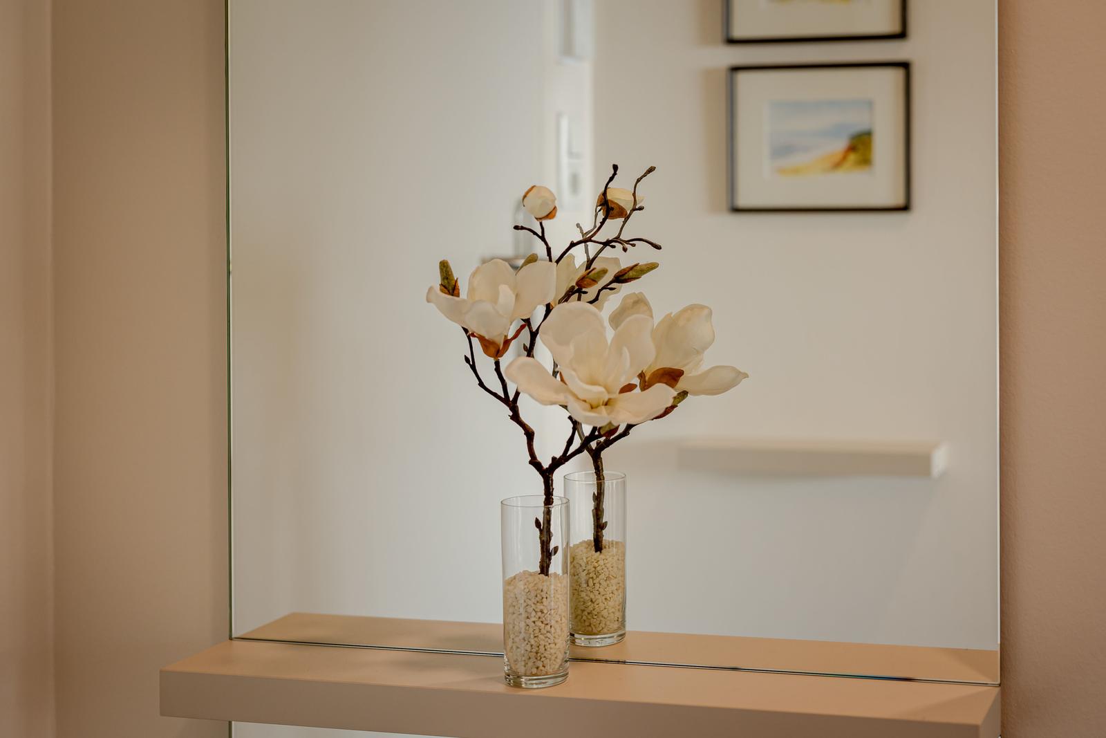 Zwei Vasen mit Magnolienblüten auf einer Ablagefläche vor einem Spiegel.